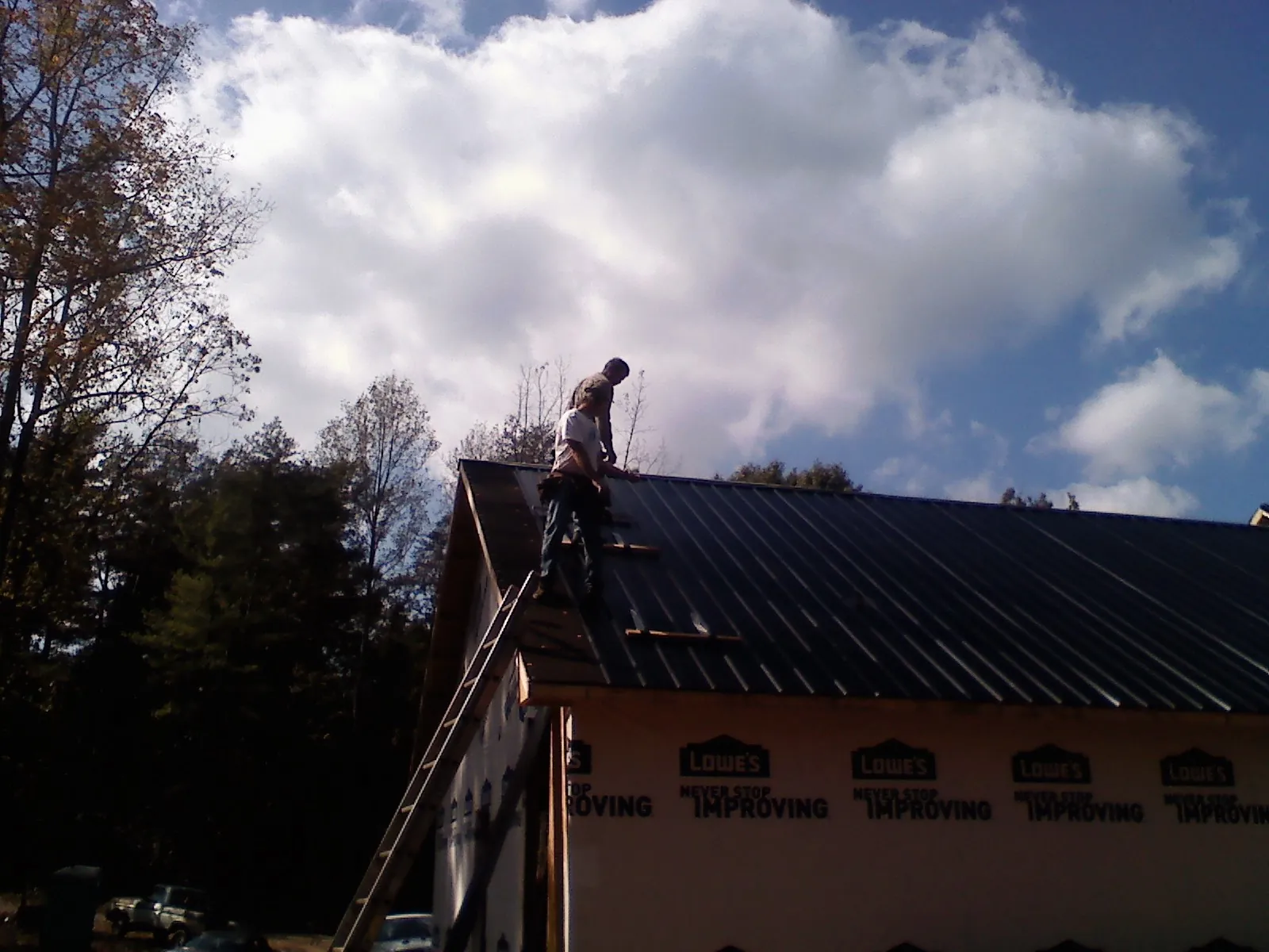 Roofer fastening dark metal panels high against a cloudy sky, from a Roof Inspection job in Lewisburg