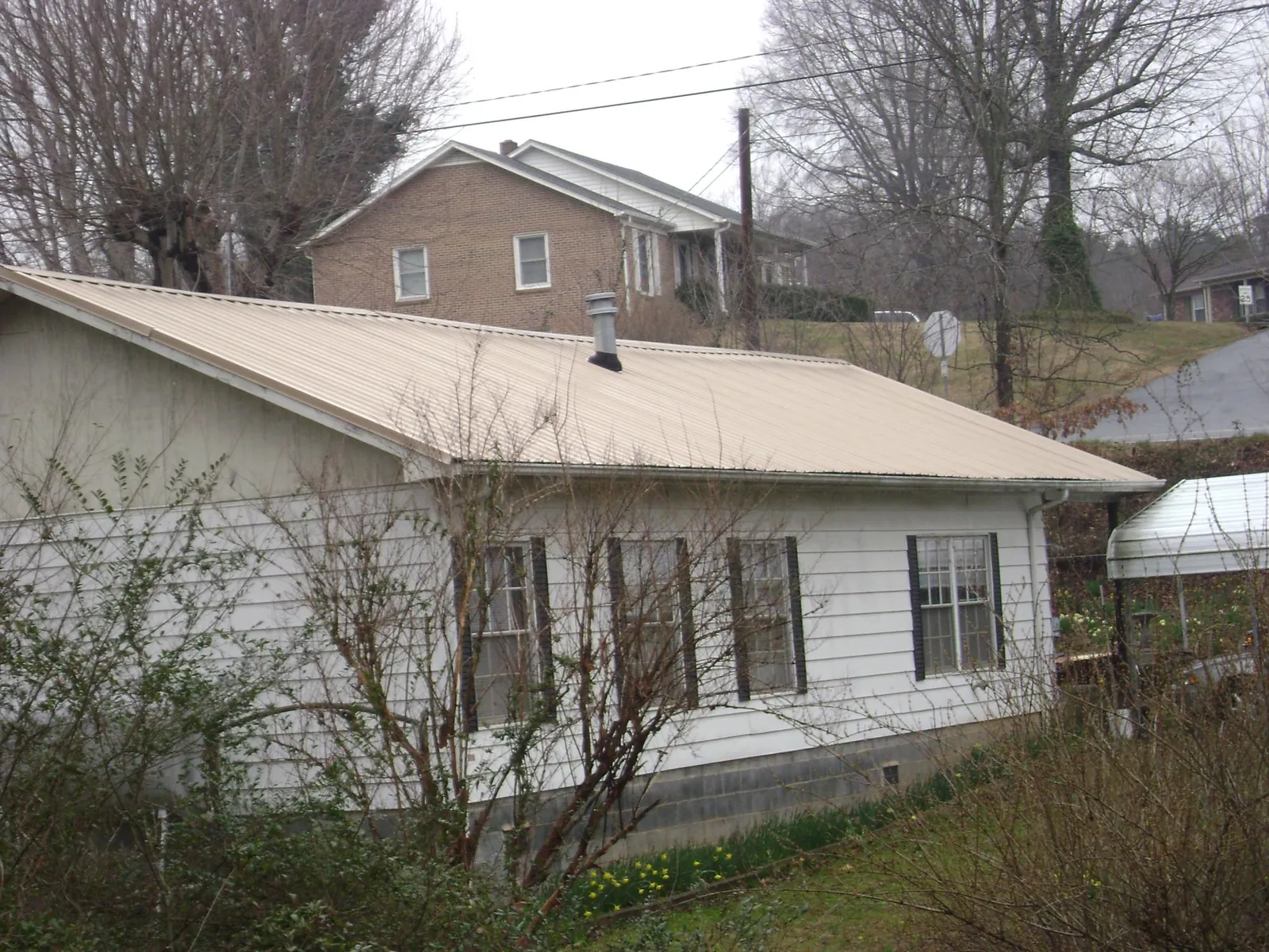 Tan metal roof on a white sided house set into a hillside — Commercial Roofing by Roofing Brothers in Lewisburg